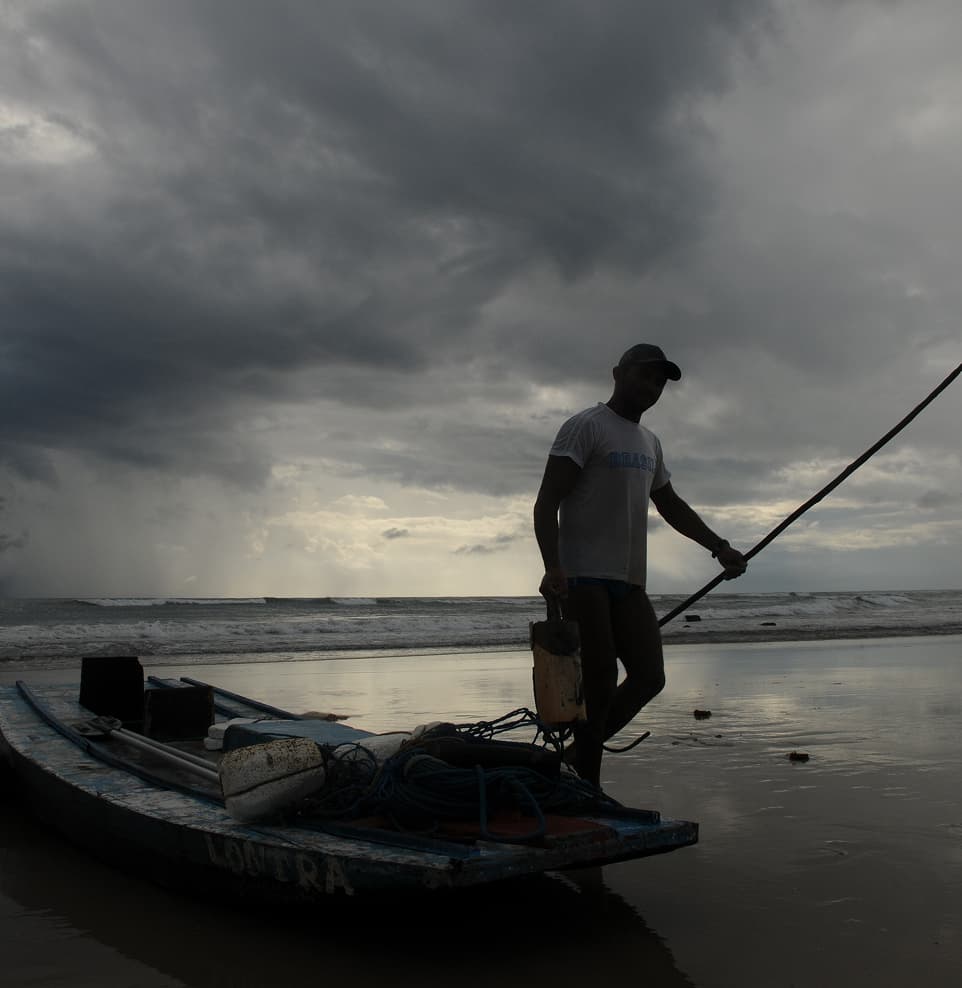 Pescador local ao lado do barco na praia de Sibaúma em manhã nublada, próximo ao Kilombo Villas