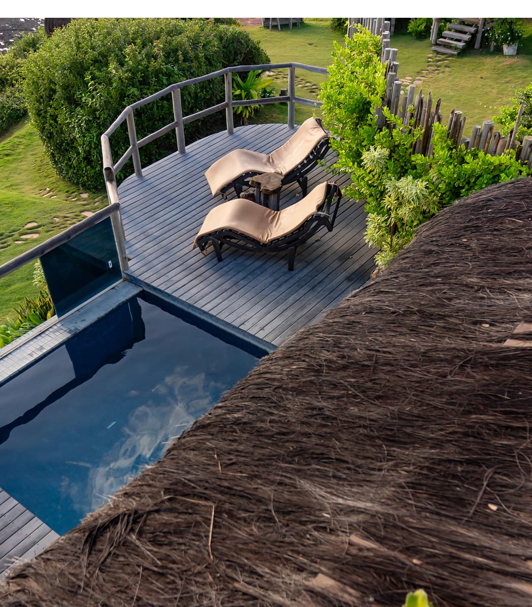 Deck de madeira com espreguiçadeiras e piscina privativa vistos do telhado de palha de uma villa do Kilombo Villas