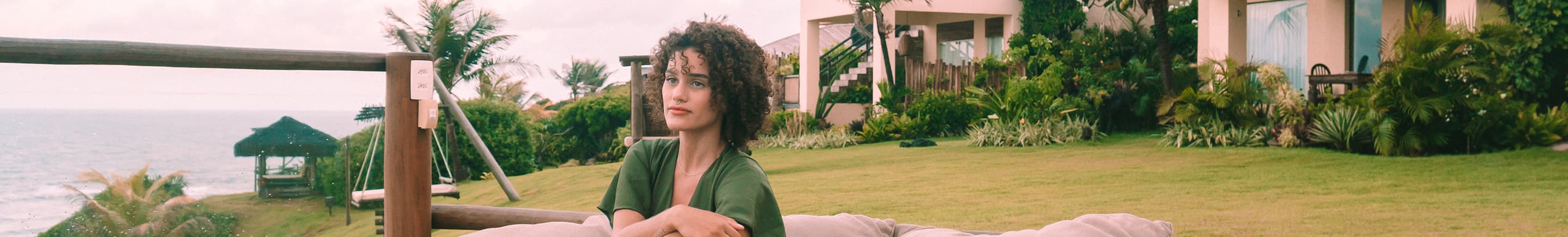 Hóspede sentada em almofadões no jardim com vista para o mar no Kilombo Villas