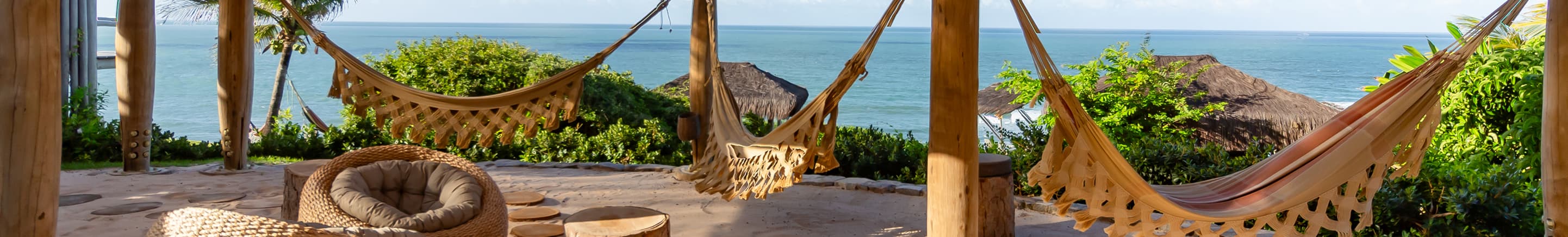 Redes e pufes de fibra natural sob pavilhão de palha com vista para o mar no Kilombo Villas