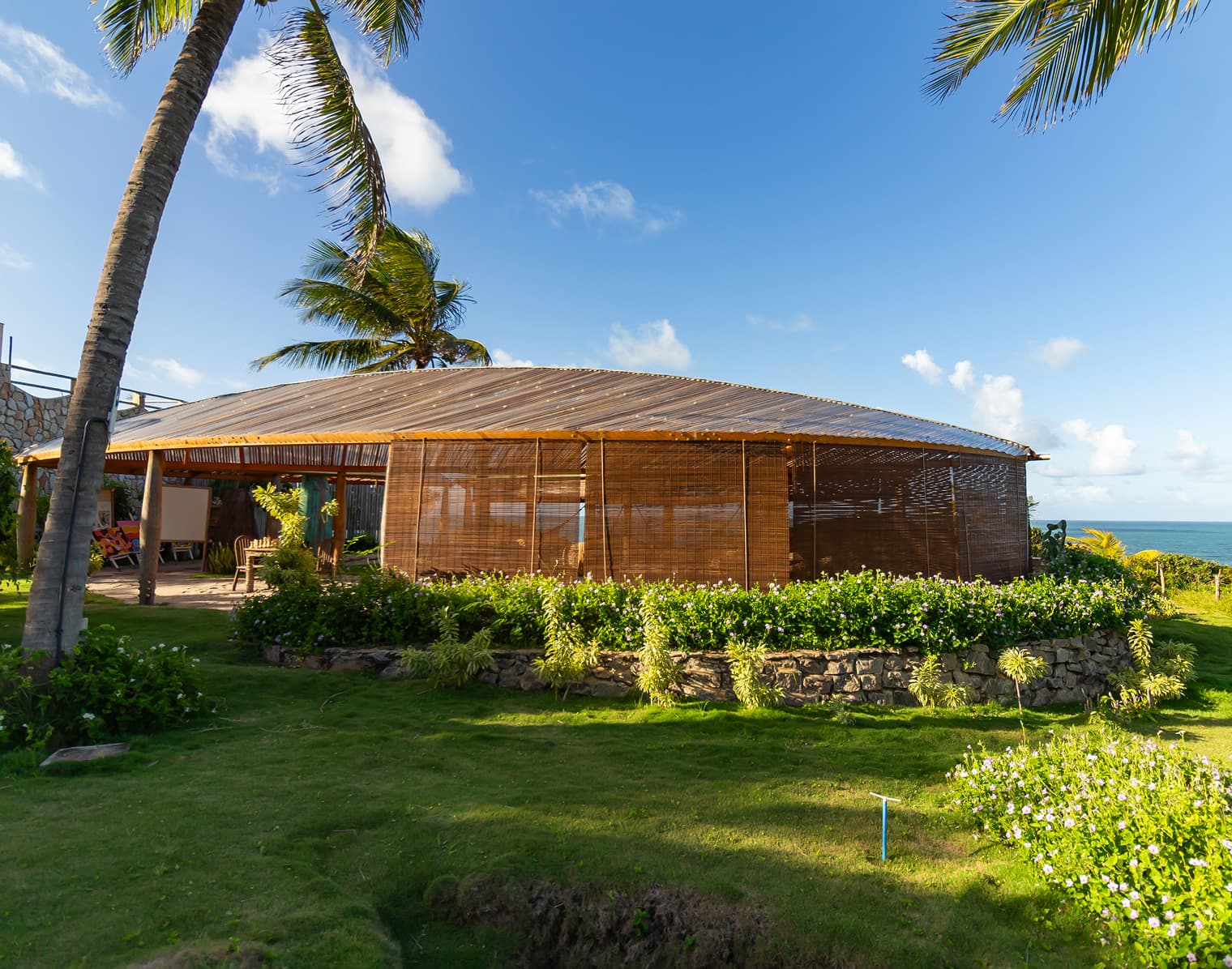 Pavilhão de bambu e palha cercado por coqueiros e jardim, à beira-mar, no Kilombo Villas