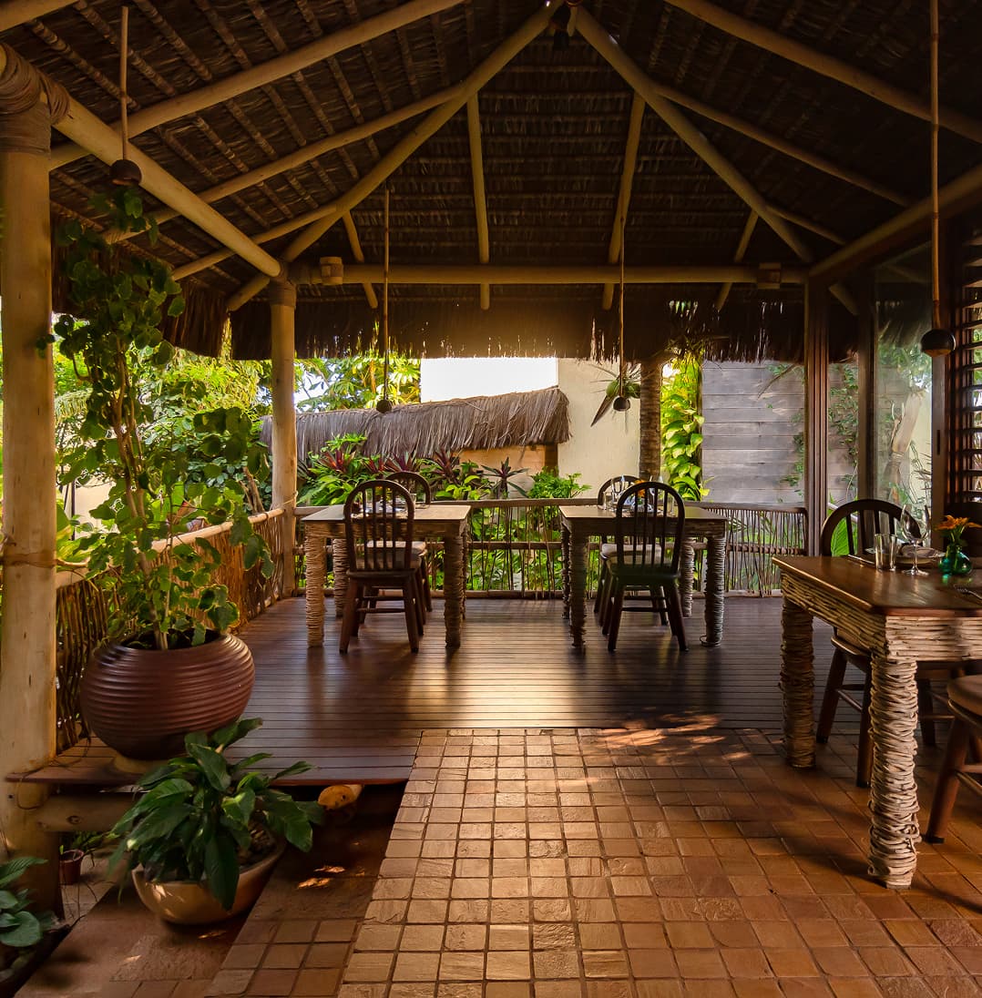 Varanda coberta de palha com mesa de jantar de madeira e plantas tropicais no Kilombo Villas