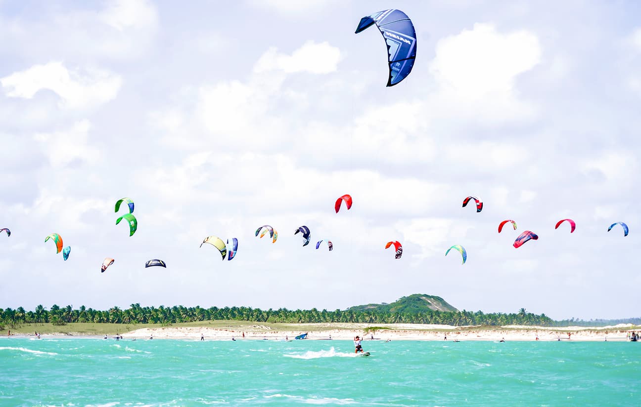 Vista aérea de kites coloridos sobrevoando a praia próxima ao Kilombo Villas em dia ensolarado