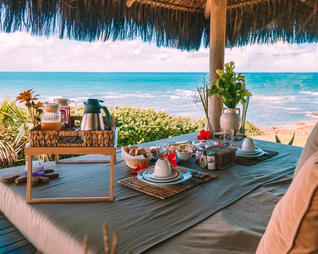 Mesa de café da manhã ao ar livre no bangalô do Kilombo Villas com vista para o oceano de Sibaúma