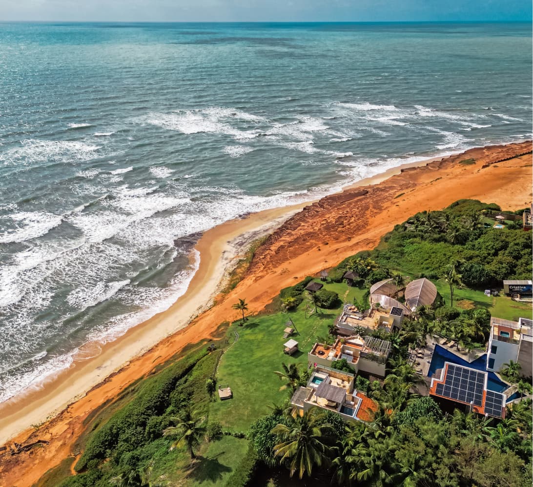 Vista aérea do Kilombo Villas com villas, jardins e falésias vermelhas à beira da praia de Sibaúma