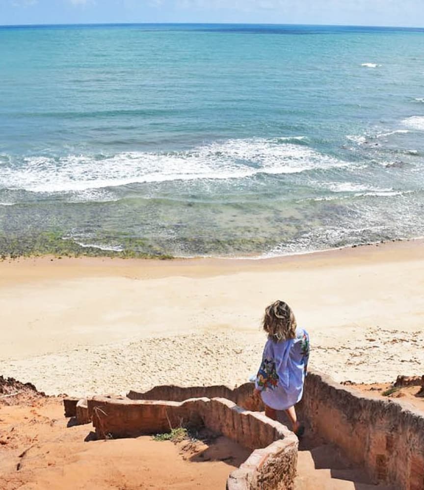 Hóspede descendo escadas de pedra em direção à praia de Sibaúma no Kilombo Villas