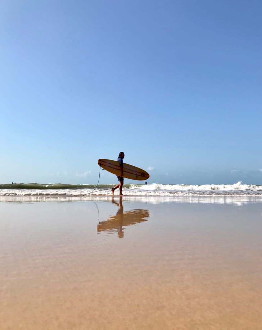 Surfista caminhando na praia de Sibaúma com uma prancha de surf embaixo do braço.