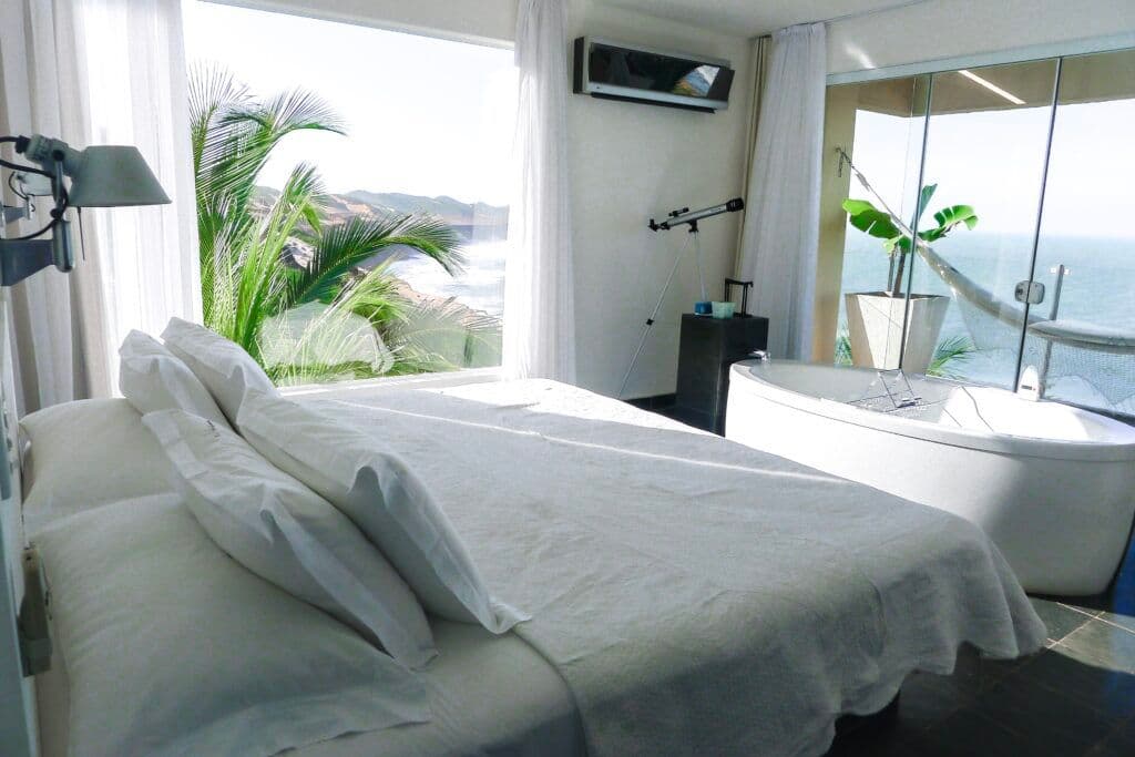 Quarto moderno com cama, banheira independente e vista panorâmica para falésias e mar