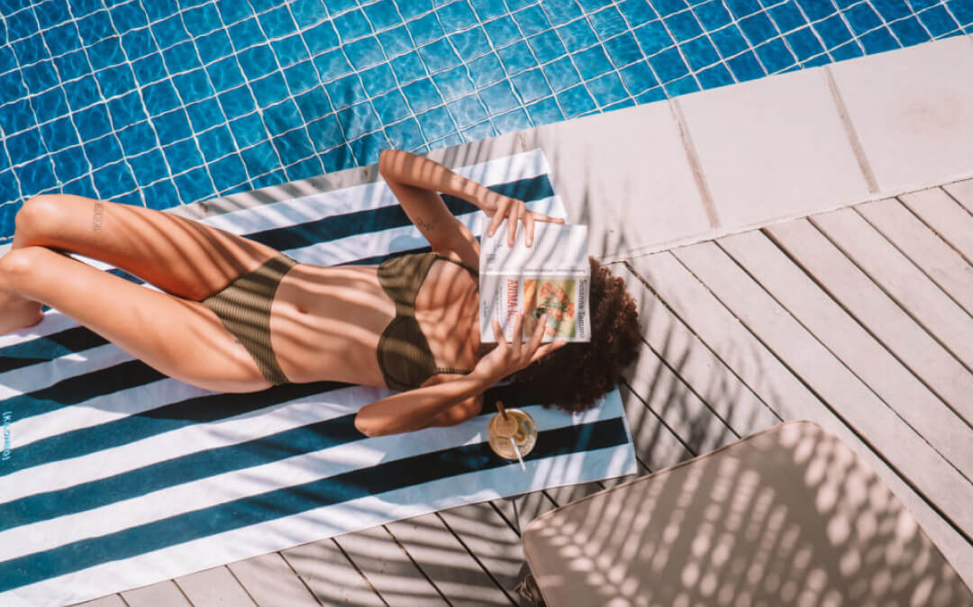 Pessoa lendo uma revista na beira da piscina do Kilombo Villas.